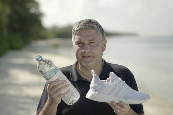 Andreas Stamm am Malediven-Strand mit verdreckter Plastikflasche und weißem Adidas-Sneaker.